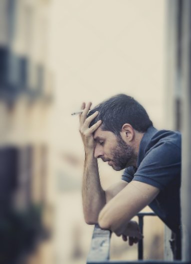 Hombre en entorno social deprimente Persona sola en un balcón fumando manifestando los efectos de un entorno que propicia la depresión